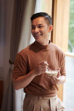 Cropped image of smiling young man eating bowl of oatmeal for breakfastの写真素材