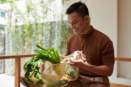 Happy young man taking out groceries he bought at local marketの写真素材