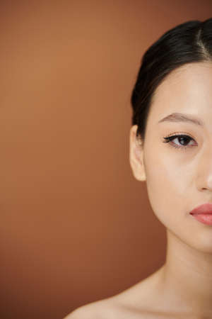 Half face of young Asian woman with eye liner and lip tint looking at cameraの写真素材