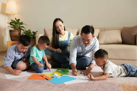 Smiling parents and their three sons drawing pictures on floor togetherの写真素材