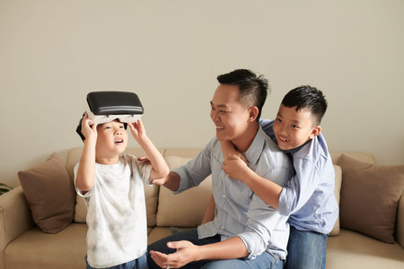 Happy father helping little son to wear virtual reality headset to play game