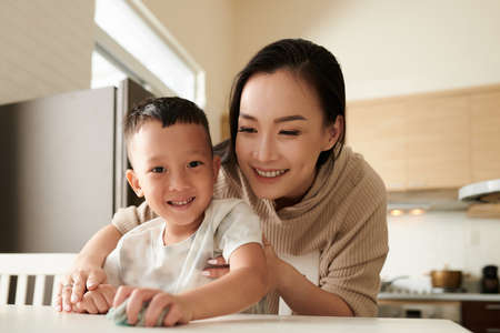 Smiling mother teaching son cleaning table after dinnerの写真素材