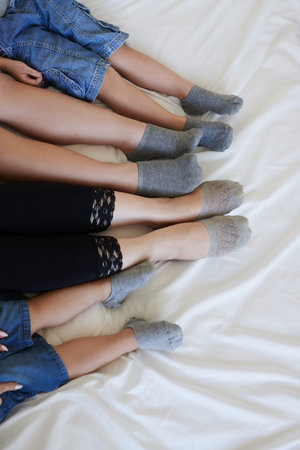 Legs of parents and three kids sitting on bed, view from above