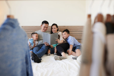 Happy parents and three children sitting on bed and reading book togetherの写真素材