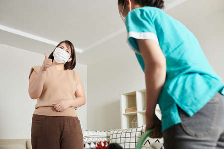 Asian woman in mask showing thumb up to cleaning service worker, she satisfying with the workの写真素材