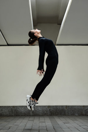 Young female dancer in black costume jumping during her modern dance alone on the street