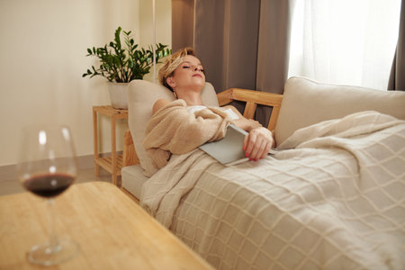 Beautiful young adult Caucasian woman taking nap on couch in living room at home after reading novel...