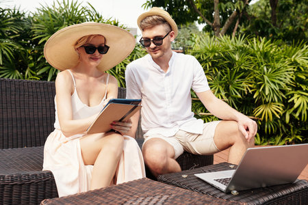 Young adult Caucasian man and woman sitting outdoors on sunny summer day working together on project...