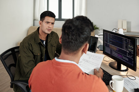 Serious software developer listening to ideas of front end developer at meeting