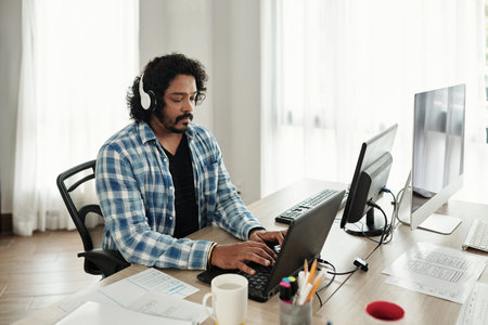 Indian front end developer enjoying music in headphone when working on website or application