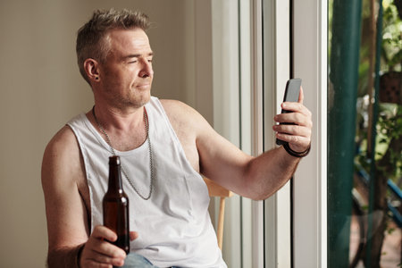 Smiling mature man drinking bottled beer when having videocall with friend