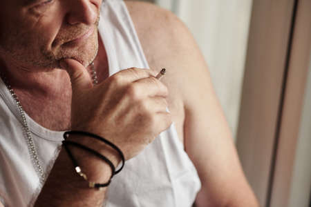Pensive mature man in white undershirt smoking cigaretteの写真素材
