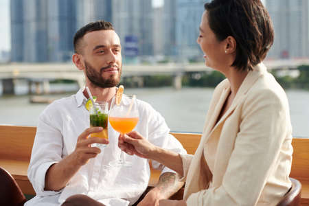 Smiling young man enjoying drinks and conversation with woman at rooftop barの写真素材
