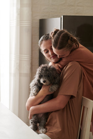 Happy young woman holding little dog when daughter hugging her from behind