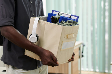 Cropped image of empoyee holding box with headphones, plant and document he brought to new office