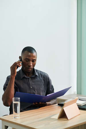 Serious frowning Black businessman talking on phone when reading details of contractの写真素材