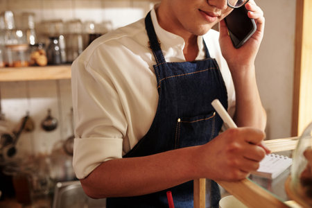 Cropped image of barista discussing details of order with customer on phoneの写真素材