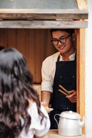 Smiling young Asian barista giving order to female customer