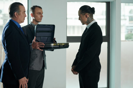 Assistant of entrepreneur showing content of briefcase to businessman at meeting