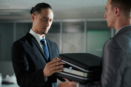 Frowning entrepreneur checking briefcase with papers and money inside