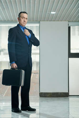 Full-length portrait of mature successful entrepreneur with briefcase adjusting necktie before important meetingの写真素材