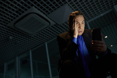 Shocked emotional businessman reading news on financial crisis on smartphoneの写真素材
