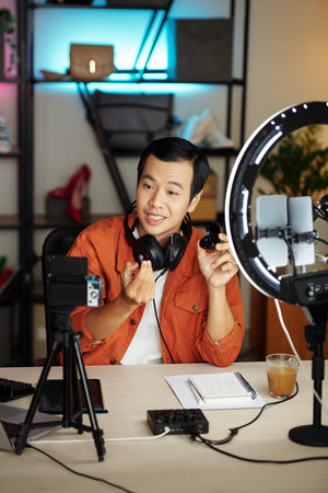 Young Asian tech blogger filming earbuds review for social media