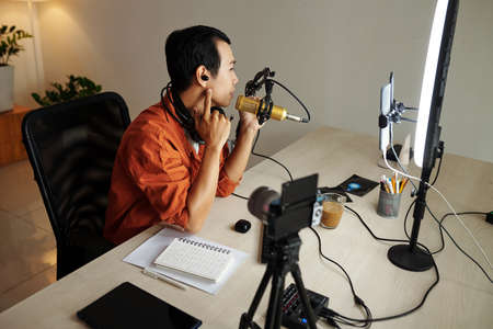 Young Vietnamese tech blogger filming review of new earbuds on smartphoneの写真素材