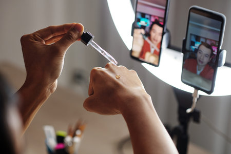 Young man filming himself dripping serum from bottle with pipette on back of hand