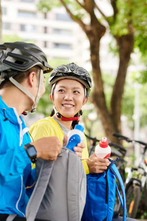 Positive young couple taking water bottles out of backpacks to drink after long bicycle rideの写真素材