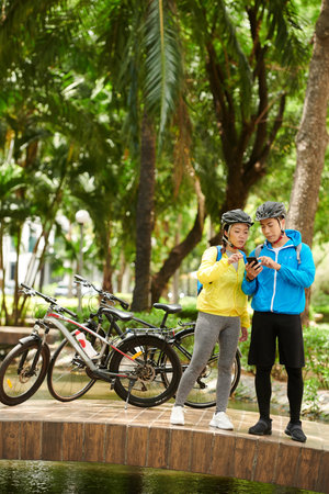 Cyclists lost in park checking map on smartphone to find entrance gate
