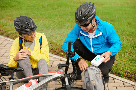 Young man taking out first aid kit from backpack to help his girlfriend who hurt knee when fell from...
