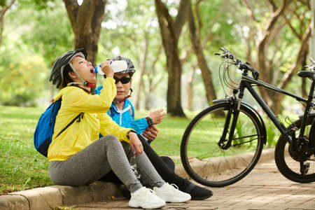 Couple tired after cycling sitting on pavement, drinking water and talkingの写真素材