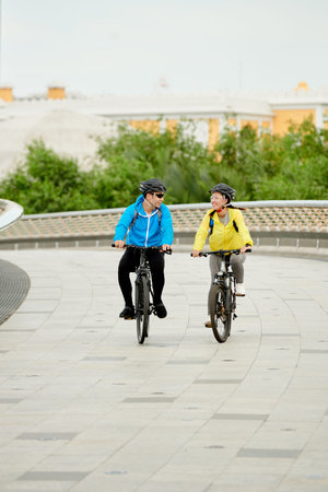 Happy couple in protective helmets riding bicycles along bridge