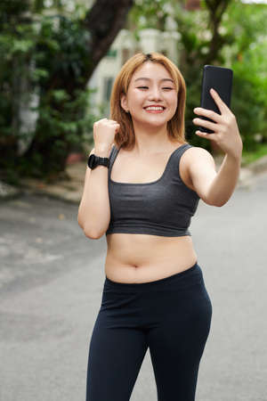 Positive fit young Asian woman taking selfie after morning jogの写真素材