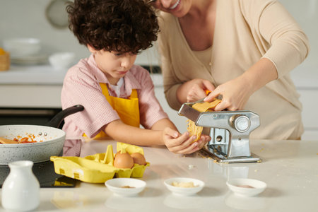 Mother and son using pasta machine to prepare spaghetti for dinner
