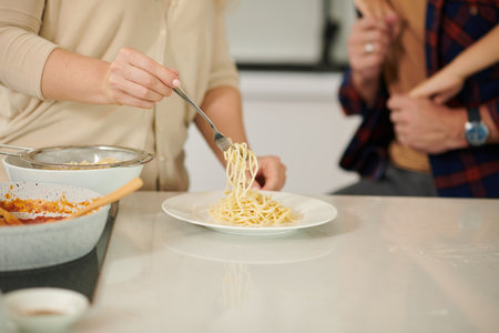 Closeup image of woman putting pasta in plates for her husband and sonの写真素材