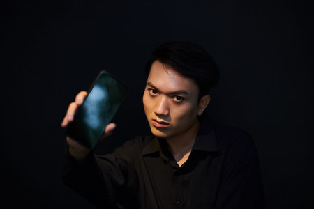 Portrait of serious internet scammer showing smartphone and looking at camera