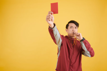 Serious football referee whistling and showing red card
