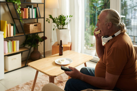 Senior man eating sandwich and watching popular show on tv at home