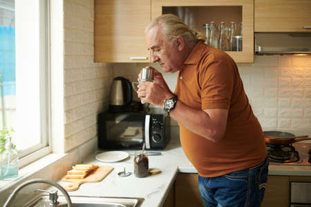 Senior man enjoying smell of grounded coffee he put in Vietnamese coffee makerの写真素材