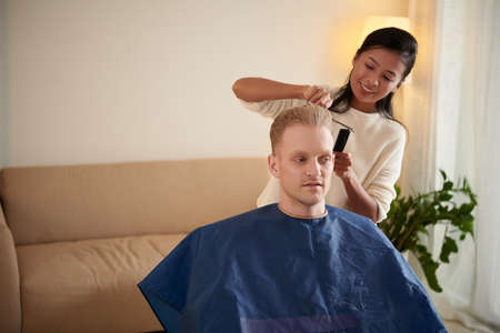 Smiling young woman cutting hair of her boyfriend in wheelchairの写真素材