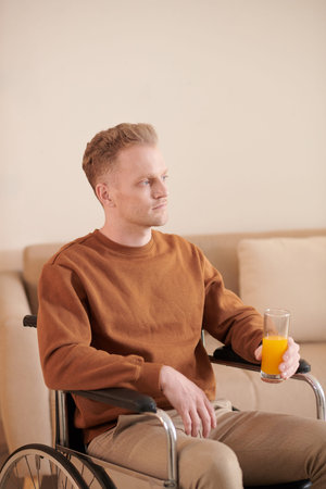 Portrait of young man in wheelchair drinking glass of fresh juice