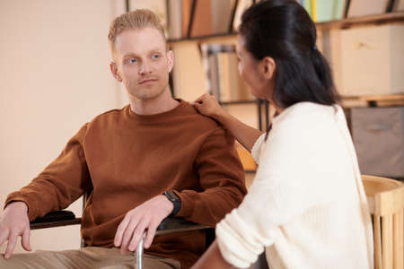 Caregiver supporting young man struggling movine in wheelchair aroud houseの写真素材