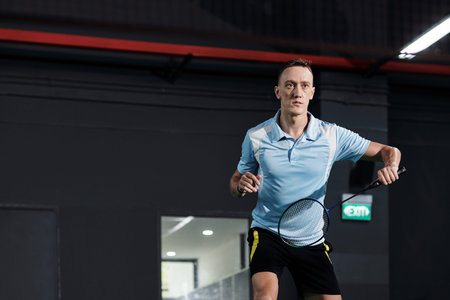 Serious young sportsman playing badminton on court