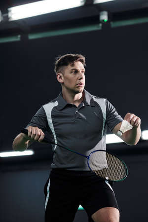 Portrait of determined sportsman serving shuttlecock when playing badminton on courtの写真素材