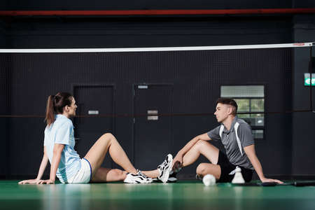 Young couple sitting on floor at net and discussing game of badmintonの写真素材