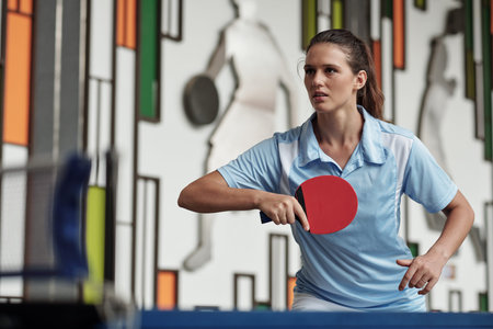 Determined young woman playing table tennis in gymの写真素材