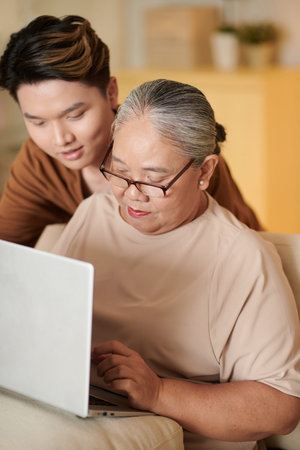 Young man teaching his grandmother how to work on laptop