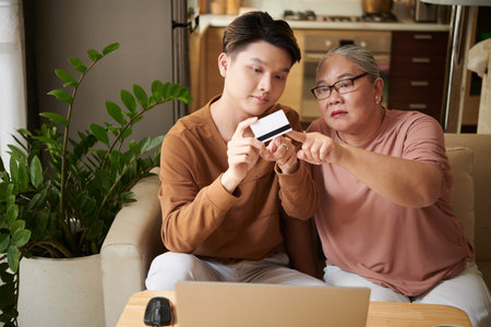 Teenage boy explaining senior woman how to pay with credit card for online purchasesの写真素材